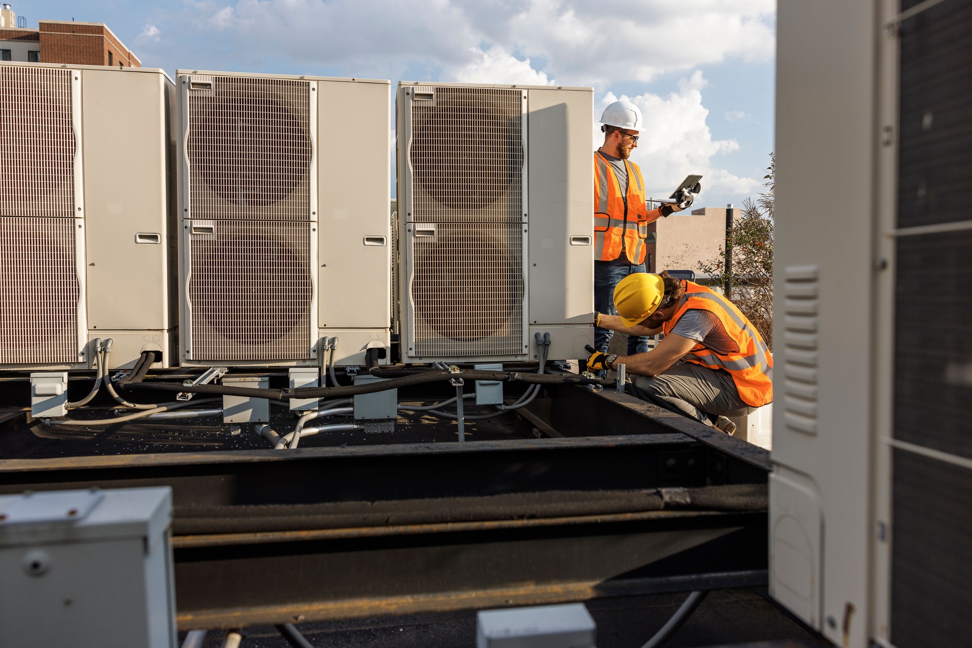 Team works together to inspect an air conditioner on a rooftop. Two construction workers are checking air condition system and logging results with a portable computer.