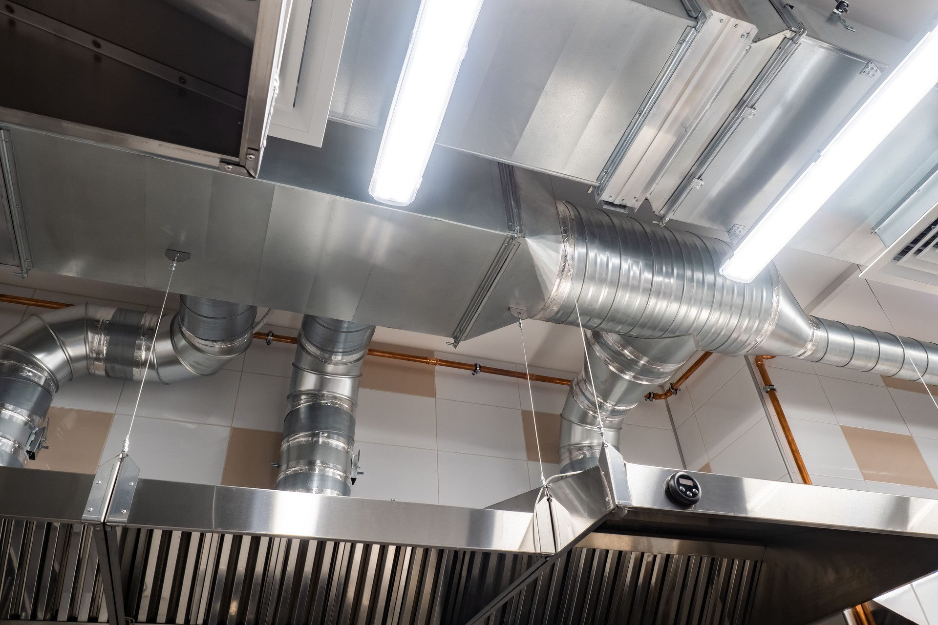 Ventilation pipes in silver insulation material. Chromed pipes hanging from ceiling inside premises. Concept is a restaurant exhaust system. Several hoods in room, bottom view. Ventilation system